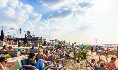 mensen zitten bij een strandtent op een terras met de voeten in het zand